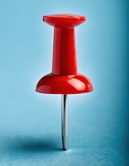 Fototapeta premium Red push pin stands prominently against a light blue background illustrating stationery use