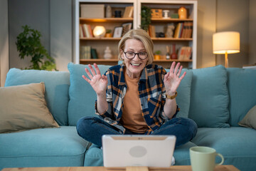 Obraz premium Happy senior woman waving during video call on tablet at home