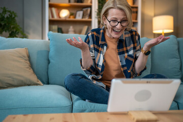 Obraz premium Excited senior woman using tablet for video call at home