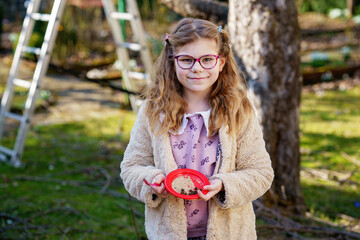 Little school girl playing with toy kitchen in garden. Happy child having fun with role activity...
