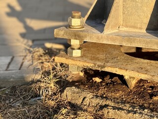 A metal pole attached to the foundation with anchor bolts and nuts. The metal surface of the post and the fastenings are in place. The support of an iron pole for lighting on the street in the park