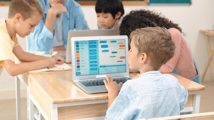 Fototapeta premium Smart caucasian boy looking at screen in STEM technology class while group of diverse student and teacher doing mind mapping. Skilled child learning coding software program or generate AI. Pedagogy.