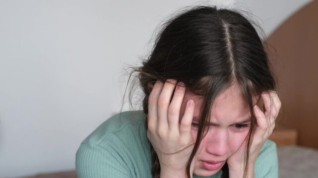 Close up face of crying preteen girl sitting on bed at home. Depressed child having bad mood. Kid feeling upset
