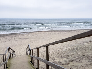 A sandy beach stretches out with wooden steps descending toward the water Waves rhythmically roll...