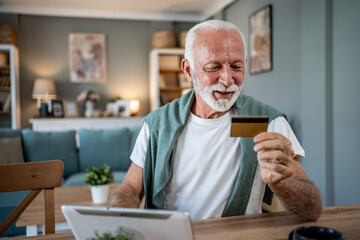 Smiling senior man using tablet and credit card for online shopping at home