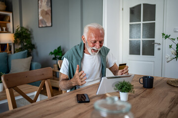 Excited senior man using tablet and credit card for online shopping at home