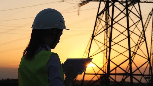 silhouette electrician engineer hand holding tablet. electric power industry high voltage. employee electrician works sunset. energy concept. electric tower high voltage. power line. work tablet sun.