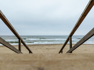 Wooden steps descend toward a tranquil beach where gentle waves lapping at the shore create a peaceful atmosphere amid a cloudy sky