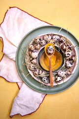 Easter table decor quail eggs on a green plate on a yellow background, top view
