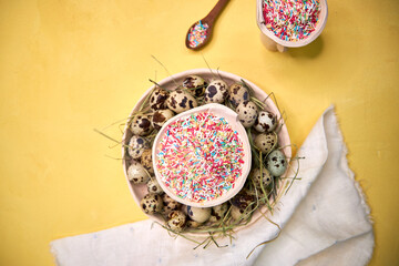 Easter table decor quail eggs on a ceramic white plate on a yellow background, closeup