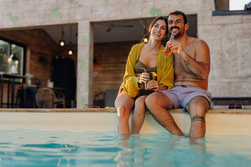 Happy couple relaxing by the pool, enjoying drinks at sunset
