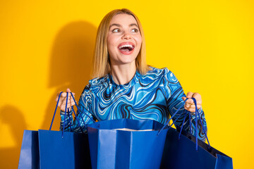 Cheerful young woman holding shopping bags against a vibrant yellow background, expressing happiness