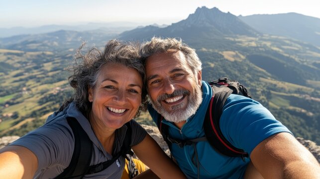 This image captures an older couple posing for a selfie on top of a mountain with stunning views.