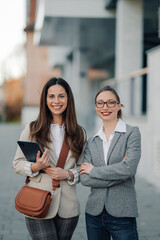 Two businesswomen smiling and holding digital tablet in urban setting