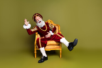 Elderly Man in Regal Costume Posing on Ornate Armchair Against Khaki