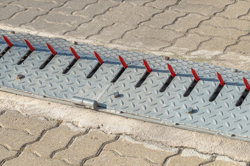 Metallic one-way spike strip with red blades, preventing vehicle entry from the wrong direction
