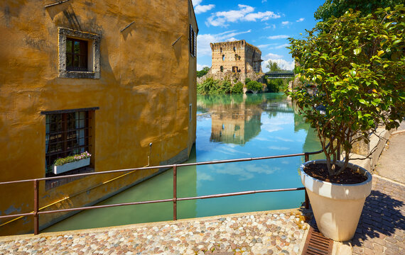 Borghetto Valeggio sul Mincio, Verona, Italy. Italian traditional village with vintage colorful houses above river. Madieval fortress ruins with bridge among ancient architecture. Summer sunny day.