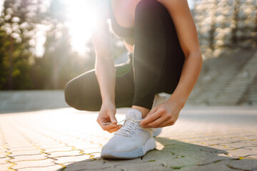 Close-up of a sporty woman tying the laces of her sneakers outdoors. Young sportswoman enjoying the...