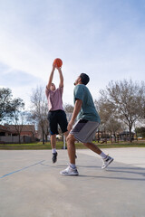 Young caucasian and latin friends playing basketball at the street court