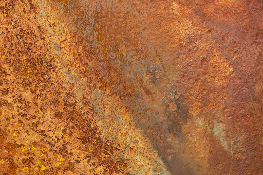 Close-up of a heavily rusted and corroded iron plate with rough texture and rich orange-brown tones. The weathered surface showcases natural patterns of oxidation and decay