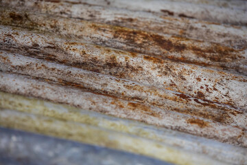 Close-up of a rusty, corrugated roof plate with weathered textures and wavy patterns. The aged metal surface showcases oxidation, creating an industrial and rugged appearance