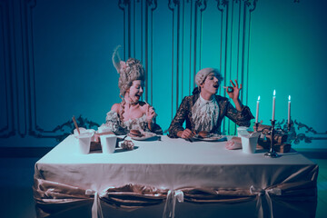 Elegant couple in baroque costumes enjoying modern food in a neon-lit ballroom setting