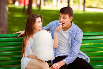 Happy young woman feeding candy floss to her boyfriend on bench at park