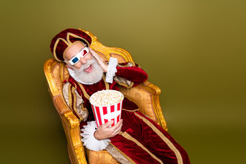 Elderly man in royal medieval attire enjoying modern cinema experience with popcorn and 3D glasses...
