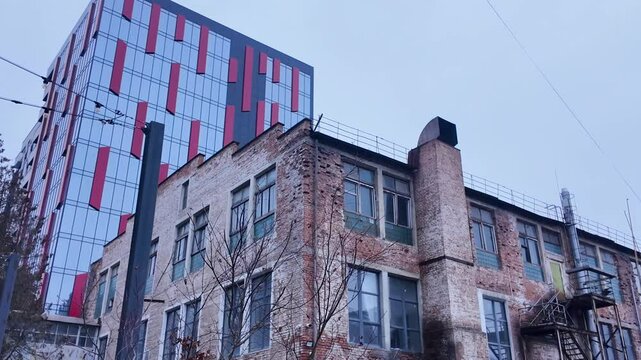 An old abandoned factory with damaged walls on the background of modern structures in the same area