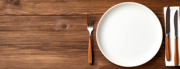 empty plate with knife and fork on a wooden table, top view.