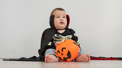 Cute caucasian boy in dracula halloween costume holding candy basket on white background. 