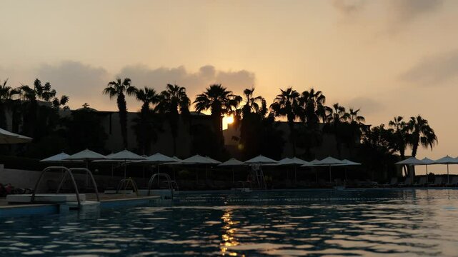 Experience a tranquil sunset above a beautiful poolside oasis adorned with palm trees
