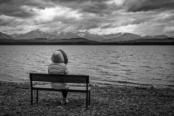 Fototapeta premium Person in jacket sitting on bench on the shore of the lake