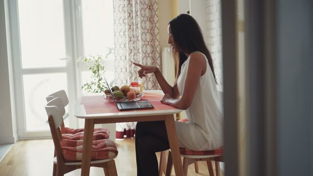 Young beautiful mulatta woman sitting at a computer and talking on video chat. At home in the kitchen. It feels happy. Shot on RED Epic Camera.