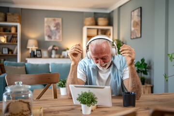 Happy senior man enjoying music with headphones and tablet at home