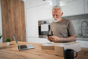Senior man using smartphone to track online order in kitchen