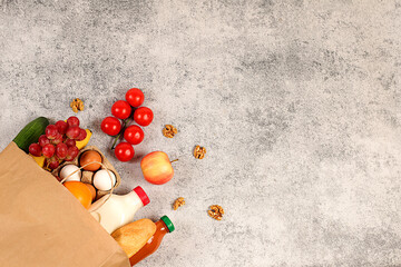 Paper bag with various natural products. Milk, eggs, baguettes, natural juice, vegetables and fruits in a ziplock bag on a concrete background, food delivery concept, advertising for a store.