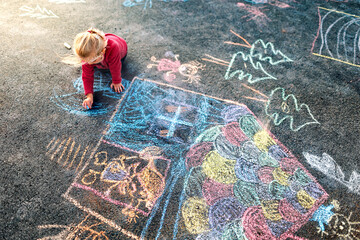 A little girl draws with chalk on asphalt. Kid’s creativity.