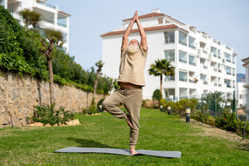 Fototapeta premium Senior man practicing yoga in the tree pose outdoors on a yoga mat