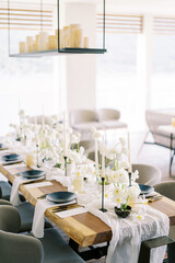 Candles stand on a hanging rack above a festive table with white flowers and black plates