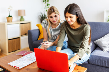 Two young happy female friends booking online their vacation trip, doing a reservation of their accommodation or flight with laptop and credit card