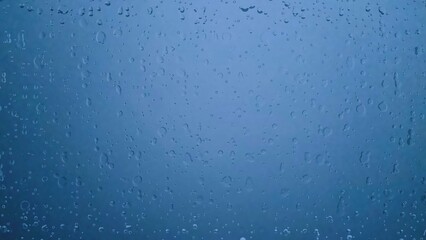 Water droplets on glass with a blue background, creating a calm and soothing atmosphere. Perfect for backgrounds, textures, or weather-related concepts.
