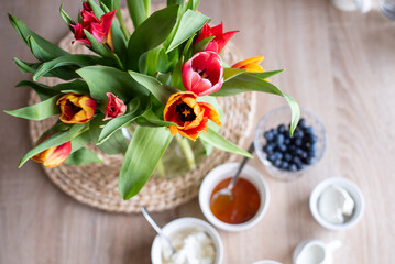 A bouquet of tulips in a glass vase in the living room and breakfast with coffee, cottage cheese and berries
