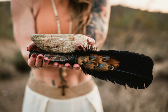 Woman in the desert holding feathers and a shell 