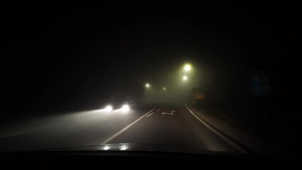 Driving in bad conditions on a foggy road at night. Front car windshield and white beam of lights. Winter weather concept, real time footage with evening lights. Nothing to see on the streets.