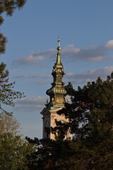 Tower with intricate architecture rises against a blue sky dotted with clouds in a serene park setting