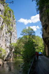 Nature lovers walking along a scenic river path between steep cliffs on a sunny day