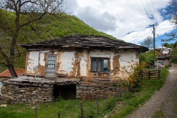 Old rustic house with weathered walls situated in a serene mountainous village during a cloudy day