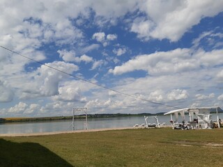 Obraz premium summer lake, wooden swing, beach, tent, deck chairs, white clouds, blue sky, reflection, forest remote, grass, summer, vacation, walk, tourist