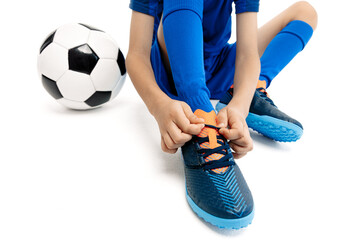 Close-up image of young boy in blue sport outfit tying his shoelaces on the floor on white background